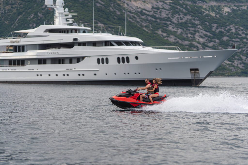 Man and woman on jet ski with superyacht Trident in the background